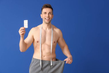 Bol elbiseli genç bir adam ve arka planda kilo verme hapları var.