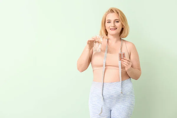 Woman with weight loss pills and water on color background