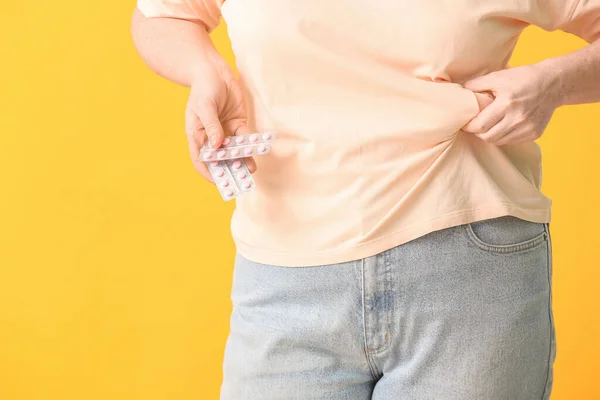 Woman with weight loss pills on color background, closeup