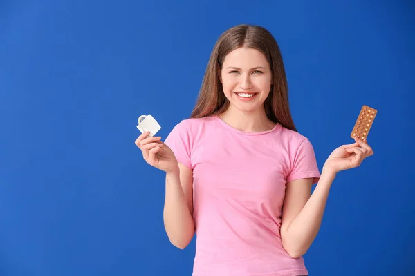有避孕药和彩色背景避孕套的年轻妇女 — 图库照片