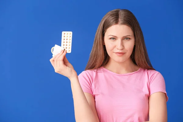 Young woman with birth control pills and condom on color background