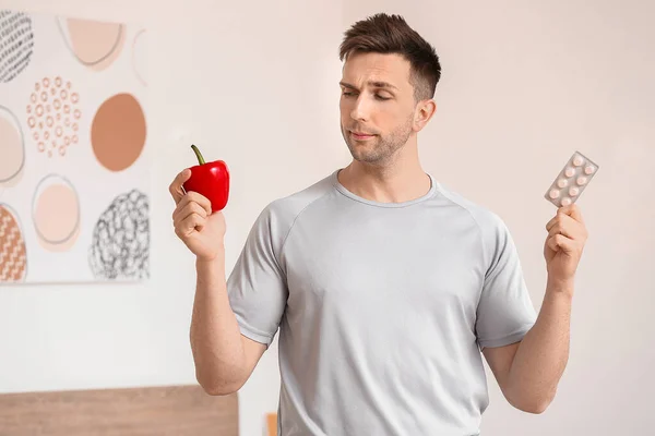 Young man with weight loss pills and pepper at home