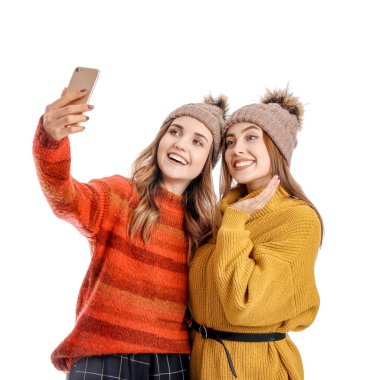 Sıcak kazaklı genç kadınlar beyaz arka planda selfie çekiyorlar.