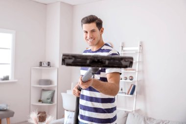 Genç adam evde yerleri süpürüyor.