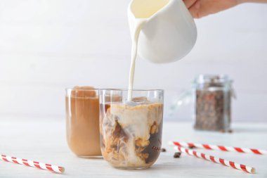 Masadaki bardakta soğuk kahveye süt dökülüyor.