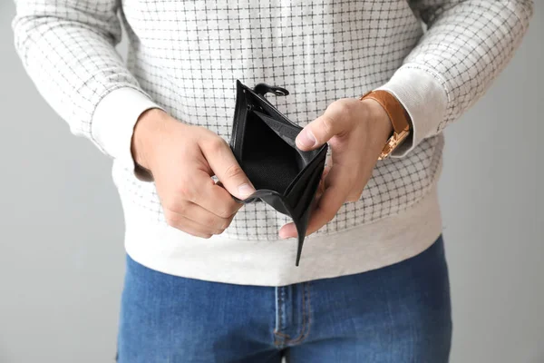 Man with empty purse on light background, closeup