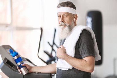 Spor salonunda elinde bir şişe su olan yaşlı bir sporcu.