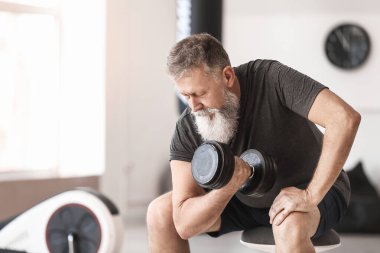Sportif yaşlı adam spor salonunda dambıllarla antrenman yapıyor.
