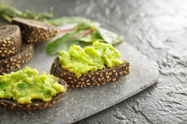 Koyu arkaplanda lezzetli avokado sandviçleri olan bir tahta.