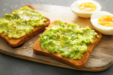 Koyu arkaplanda lezzetli avokado sandviçleri olan bir tahta.