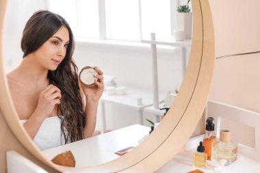 Güzel genç bir kadın evde saçına hindistan cevizi yağı sürüyor.