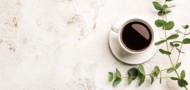 Hafif arkaplanda bir fincan sıcak kahve ve okaliptüs dalı.