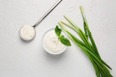 Beyaz arka planda lezzetli ekşi krema, kaşık ve yeşil soğanlı kase.