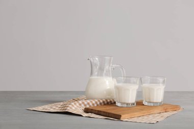 Gri arka planda taze süt bulunan cam eşyalar.
