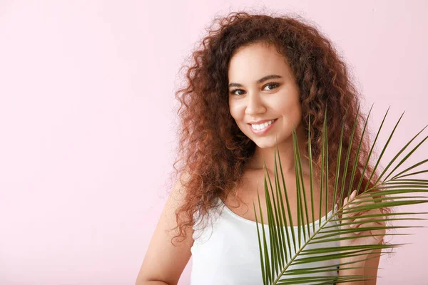 Beautiful young African-American woman with healthy skin and tropical leaf on color background