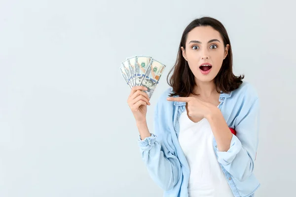 Surprised young woman with money on light background