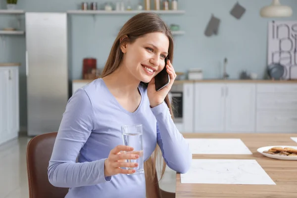 美しい妊娠中の女性と水のガラスキッチンで電話で話す — ストック写真