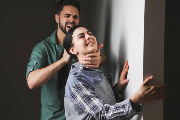 Angry husband trying to kill his wife indoors. Concept of domestic violence