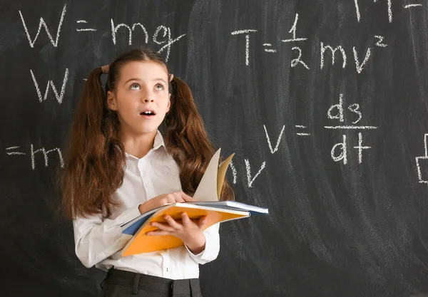 Thoughtful little girl near blackboard at physics lesson in classroom