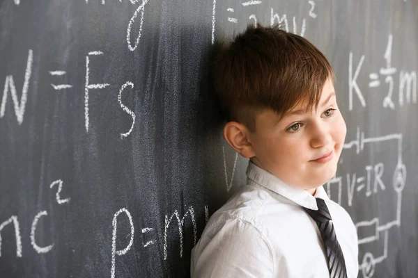 Cute little boy near blackboard at physics lesson in classroom