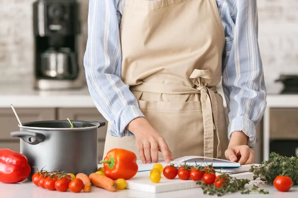 Woman with cook book preparing food in kitchen