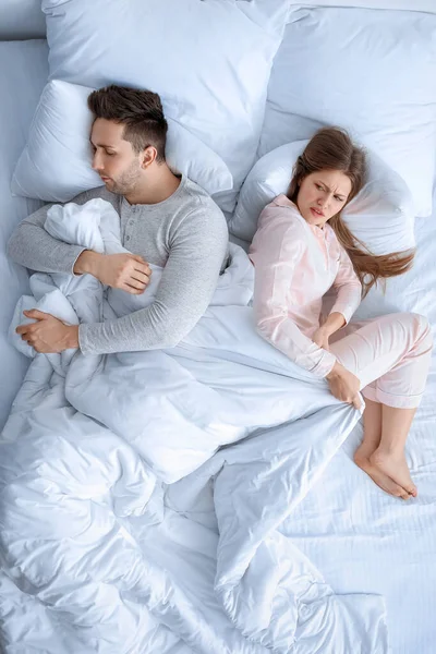 Young couple fighting for blanket in bed