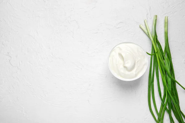 Bowl with tasty sour cream and green onion on white table