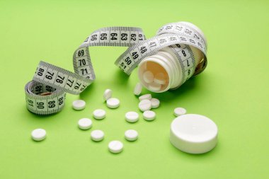 Kilo verme haplarıyla dolu bir şişe ve arka planda mezura.