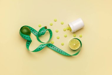 Kilo verme haplarıyla dolu bir şişe, limon meyvesi ve renkli arka planda mezura.