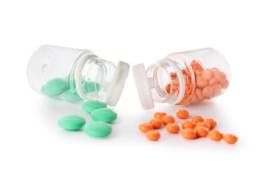 Beyaz arka planda farklı haplar bulunan şişeler.