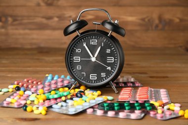 Ahşap arka planda farklı haplar bulunan çalar saat.