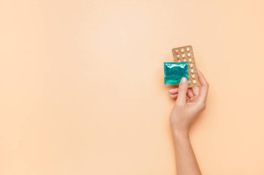 Doğum kontrol hapları ve renkli arka planda prezervatifli bir kadın eli.