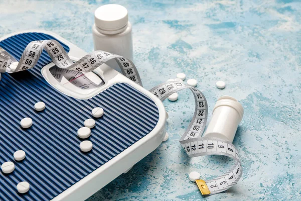 Bottles with weight loss pills, scales and measuring tape on color background