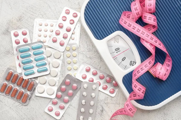 Weight loss pills, scales and measuring tape on grey background