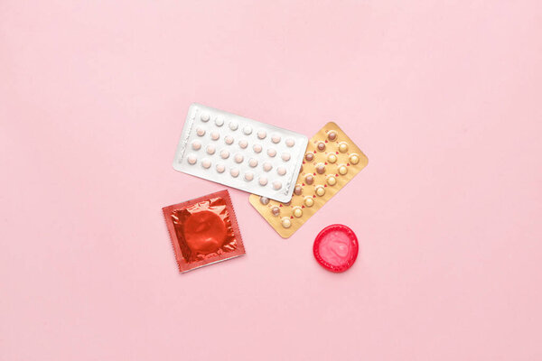Противозачаточные таблетки и презервативы на цветном фоне
