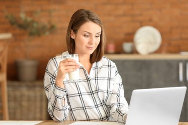 Evde süt içen dizüstü bilgisayarı olan güzel genç bir kadın.