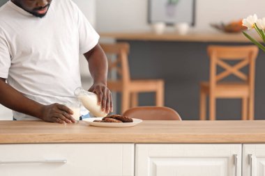 Afro-Amerikalı adam mutfakta süt içiyor.