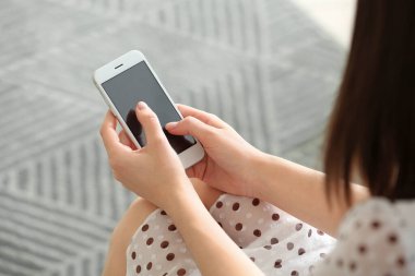 Evinde cep telefonu olan güzel genç bir kadın, yakın plan.