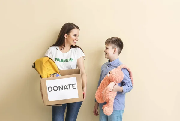 Volunteer with donations for orphans and little child on color background