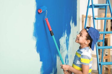Küçük Afro-Amerikalı çocuk odada duvar boyuyor.