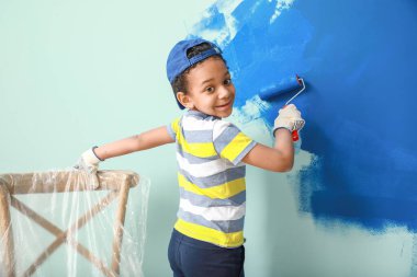Küçük Afro-Amerikalı çocuk odada duvar boyuyor.