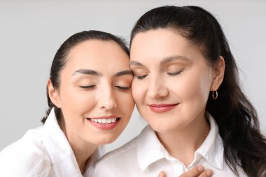 Gri arka planda yetişkin kız ve annesinin portresi