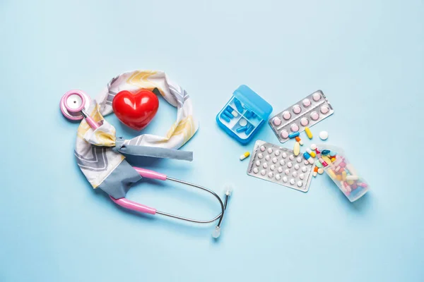 Stethoscope with cover, heart and pills on color background