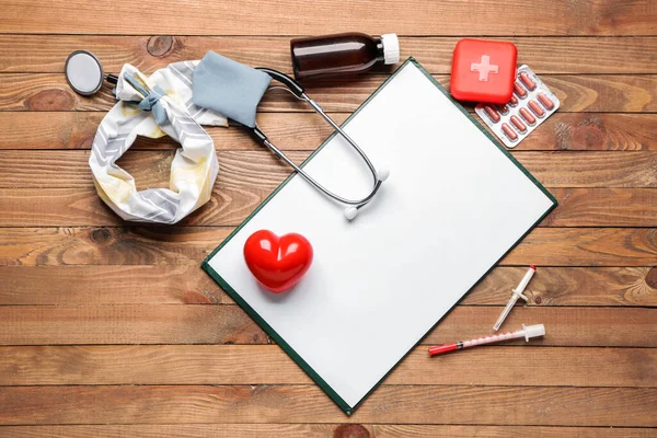 Stethoscope with cover, heart, clipboard and supplies on wooden background