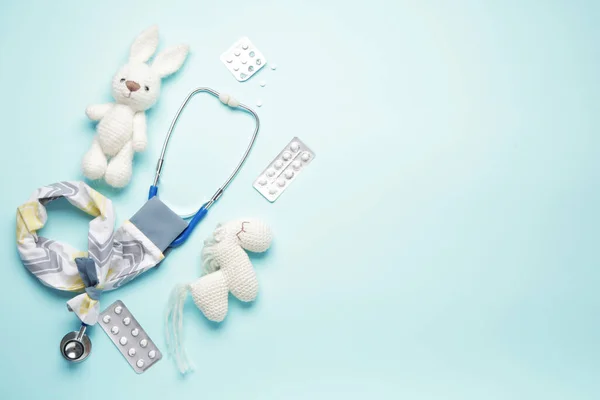 Stethoscope with cover, toys and pills on color background