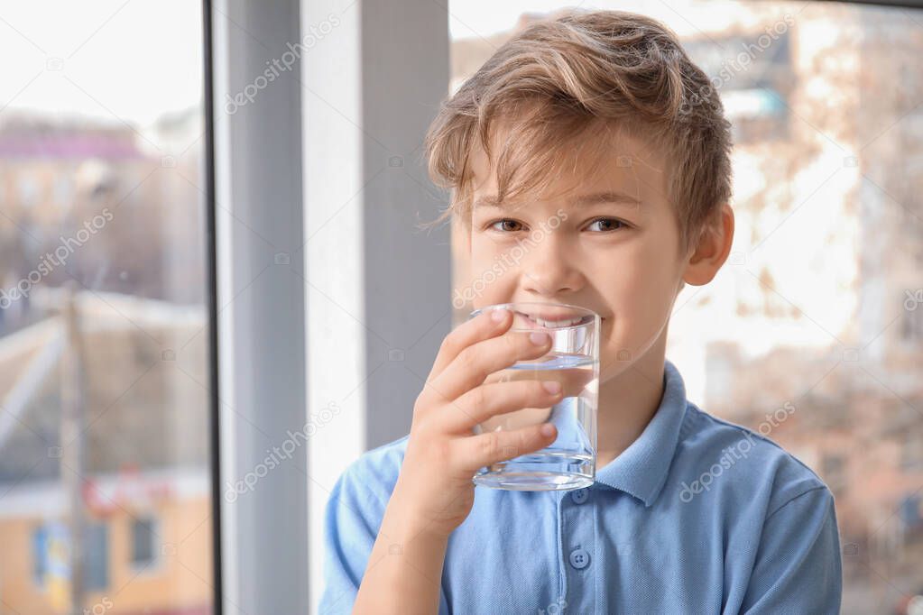Cute little boy drinking water near window