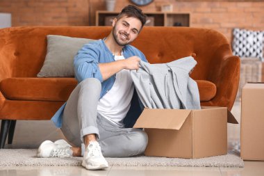 Evde yeni kıyafetlerle birlikte kutuları açan genç adam.