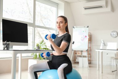 Genç bir kadın ofiste spor yaparken spor yapıyor.
