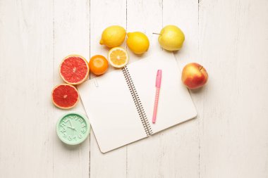 Masanın üzerinde taze meyve ve saat olan defter.