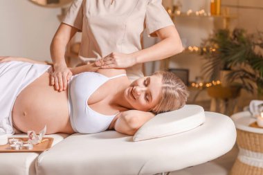Genç hamile kadın spa salonunda masaj yaptırıyor.